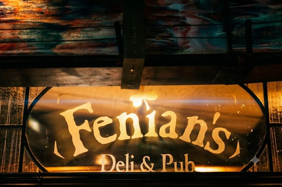 The old etched-glass sign over the bar, Fenian's Deli & Pub, lit amber from behind