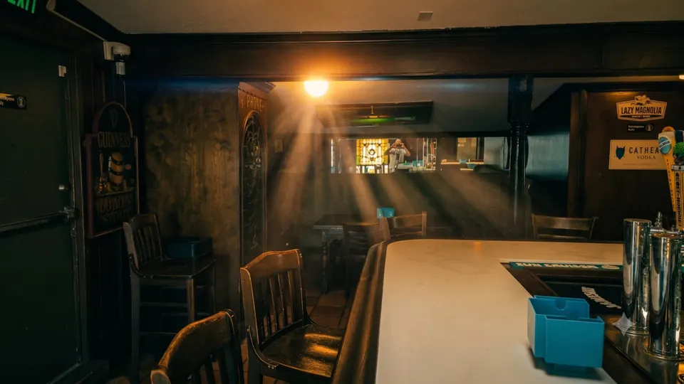 A shaft of late sun across the empty bar: stools at the white counter, a Guinness sign on the wall